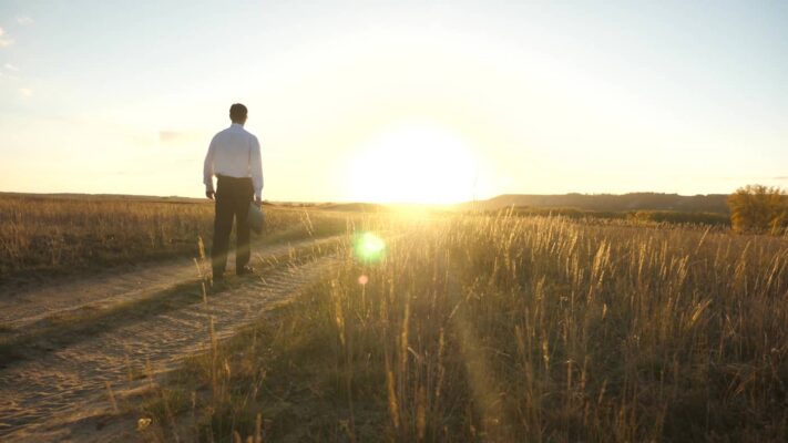 Ein Mann im Anzug geht der Sonne entgegen und signalisiert den Sinn in der Arbeit durch das Unternehmensleitbild.