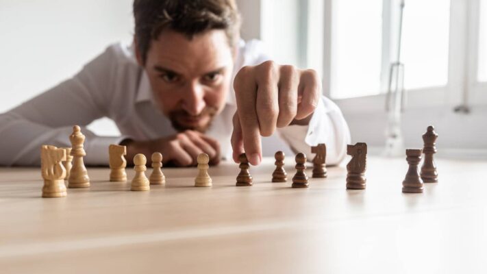 Mann mit weißen Hemd wählt auf einem Tisch stehende Schachfiguren die Maßnahmen gegen Fachkräftemangel symbolisieren.
